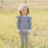 Little girl in a Blue Meadow Ruffle French Terry Set standing in a grassy field, showing off the charming floral design.