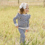 Cheerful child wearing Blue Meadow Ruffle French Terry Set, playing in a sunny field with a big bow in her hair.