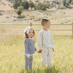 Two children joyfully wearing Blue Meadow Ruffle French Terry Set, enjoying a sunny day in a field.