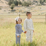 Two children joyfully wearing Blue Meadow Ruffle French Terry Set, enjoying a sunny day in a field.