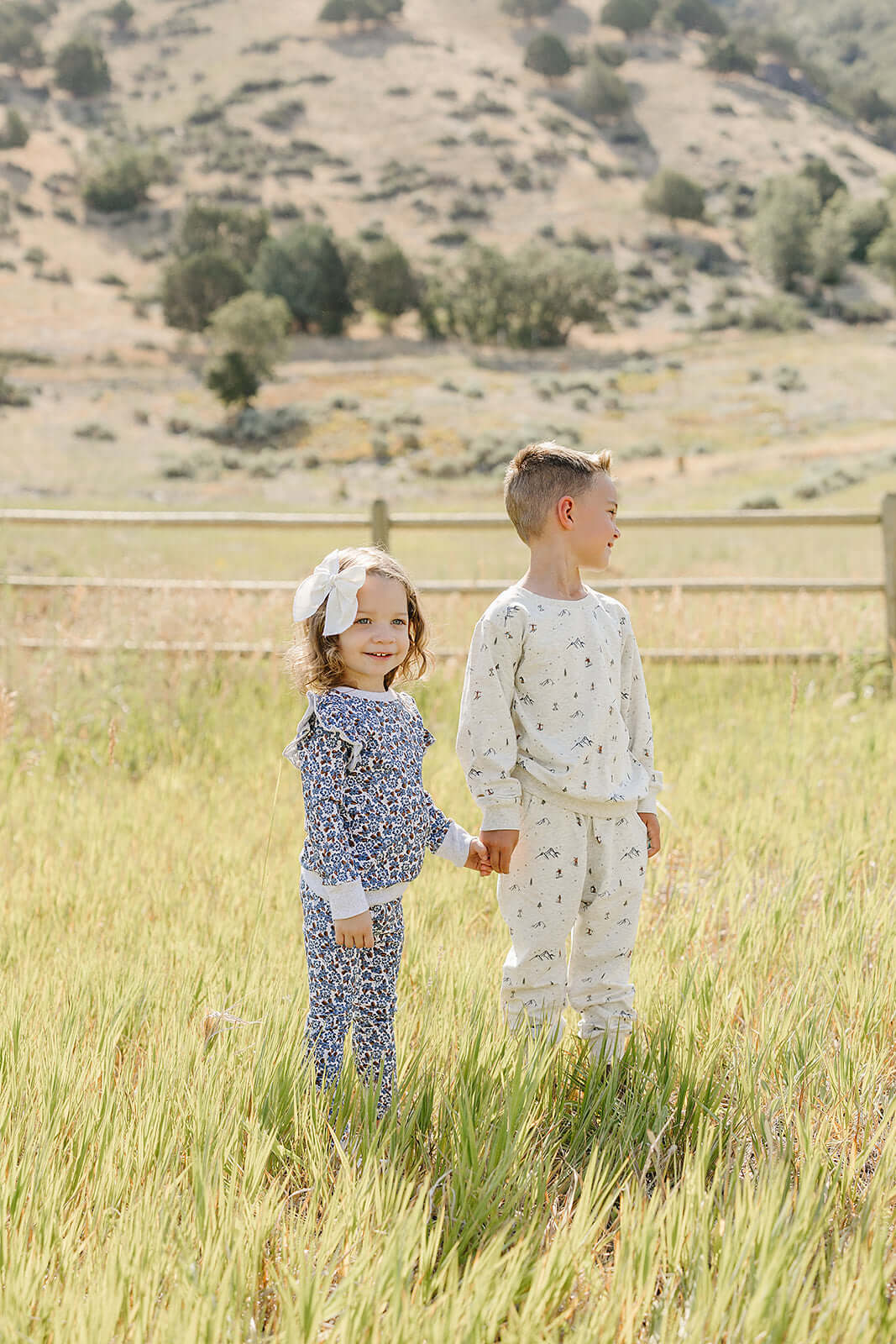 Two children joyfully wearing Blue Meadow Ruffle French Terry Set, enjoying a sunny day in a field.