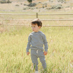 A child exploring a grassy field wearing a Charcoal Stripe Ribbed Hooded Set, perfect for outdoor adventures.