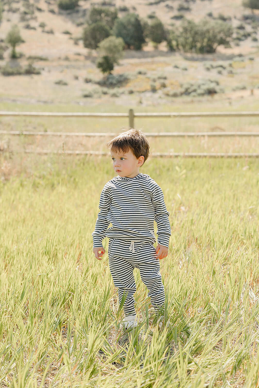 A child exploring a grassy field wearing a Charcoal Stripe Ribbed Hooded Set, perfect for outdoor adventures.