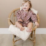 Adorable baby sitting in a chair wearing an Antique Floral Bubble Romper with ruffles and floral print.