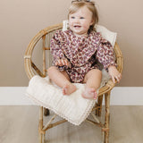 Adorable baby sitting in a chair wearing an Antique Floral Bubble Romper with ruffles and floral print.
