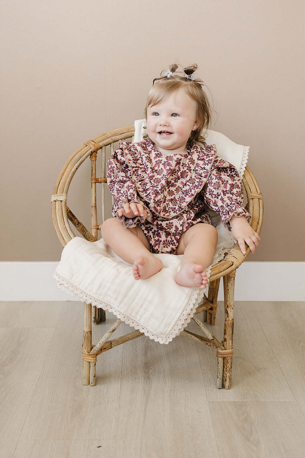 Adorable baby sitting in a chair wearing an Antique Floral Bubble Romper with ruffles and floral print.