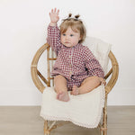 Cute baby wearing Red Gingham Peter Pan Collar Bloomer Set, sitting in a chair and raising a hand.