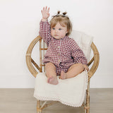 Cute baby wearing Red Gingham Peter Pan Collar Bloomer Set, sitting in a chair and raising a hand.