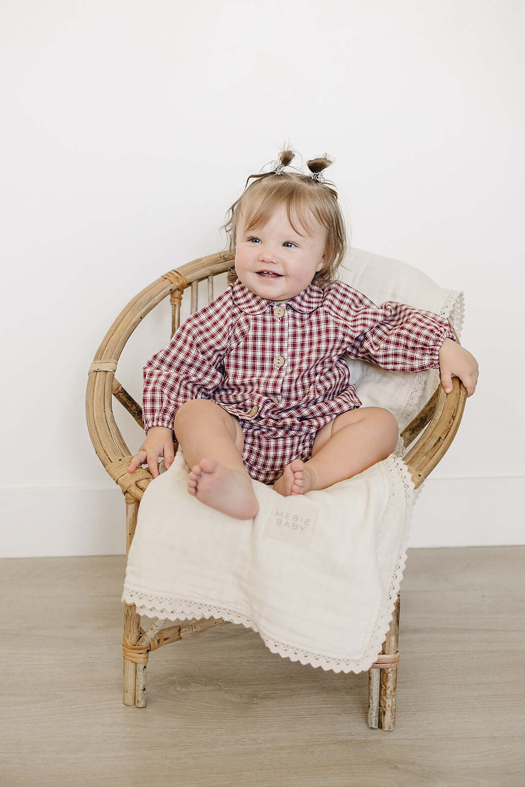 Adorable baby wearing a Red Gingham Peter Pan Collar Bloomer Set, sitting on a chair and smiling