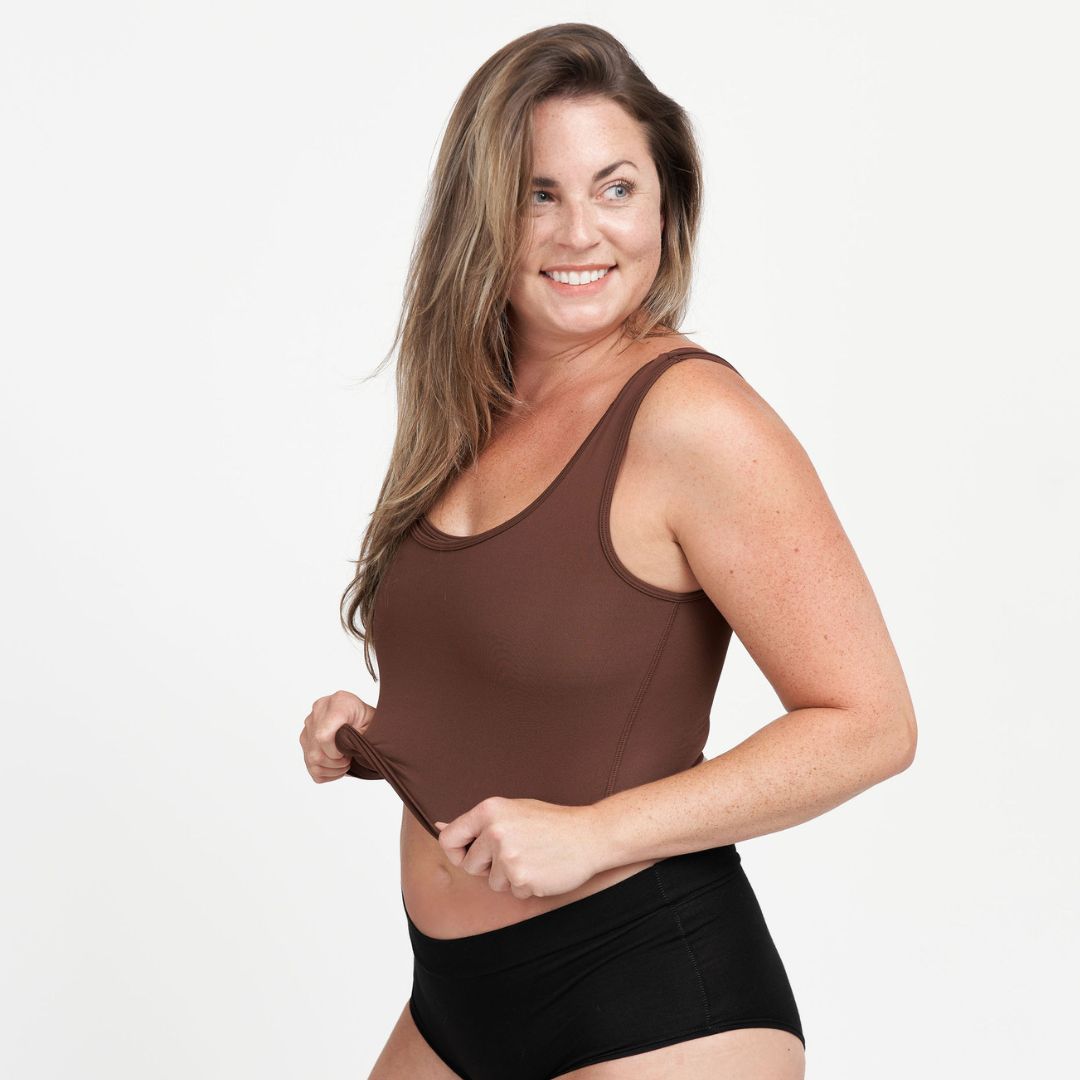 Woman wearing a brown tank top and black underwear on a white background