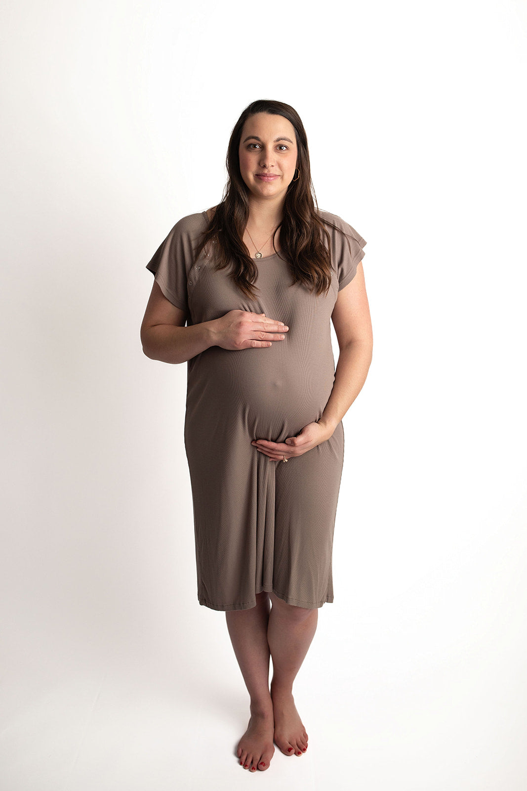 Pregnant woman wearing a Ribbed Cocoa Brown Labor & Delivery Gown, standing and holding her belly.