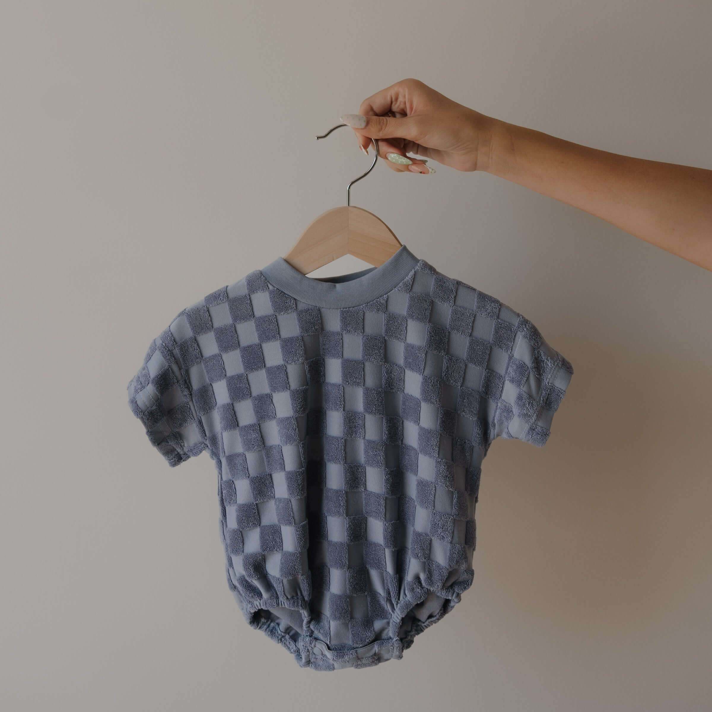Checkered baby romper on a hanger against a plain background