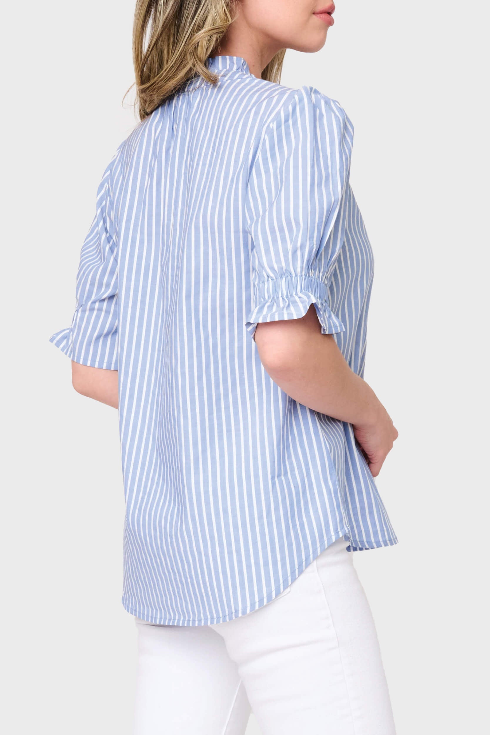 Woman wearing a blue and white striped shirt with rolled-up sleeves on a plain background