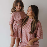 Two people wearing matching pink checkered outfits against a plain background