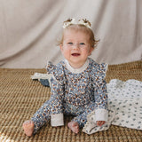 Adorable baby in Blue Meadow Ruffle French Terry Set, smiling and sitting comfortably on a woven mat.