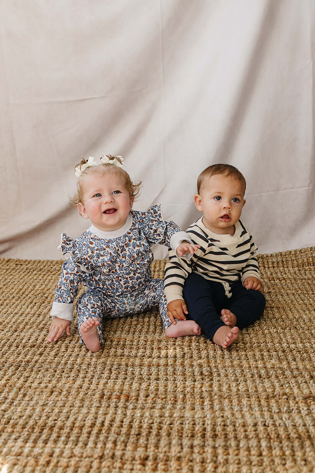 Two adorable babies wearing Blue Meadow Ruffle French Terry Set and cozy outfits, happy and ready for playtime.