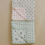 Tee Time + Green Gingham Muslin Quilt | Indulge your little one in the cozy comfort of our Muslin Quilt. Crafted from the same fabric as our beloved muslin swaddles, this four-layer quilt offers warmth and softness for a restful sleep. Our neutral colors