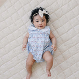 Adorable baby wearing Blue Meadow Bubble Romper with a bow on a soft quilt, perfect for sunny days.