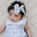 Sweet baby wearing a Blue Meadow Bubble Romper with delicate red flowers and a light blue bow headband.