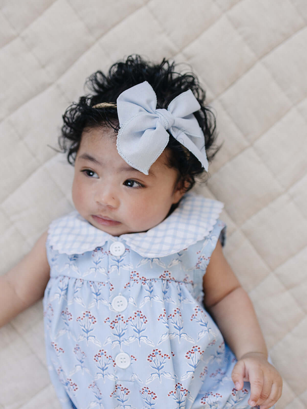 Sweet baby wearing a Blue Meadow Bubble Romper with delicate red flowers and a light blue bow headband.