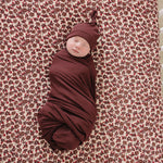 Deep Violet Ribbed Bamboo Newborn Knot Hat on a swaddled baby against a floral background.