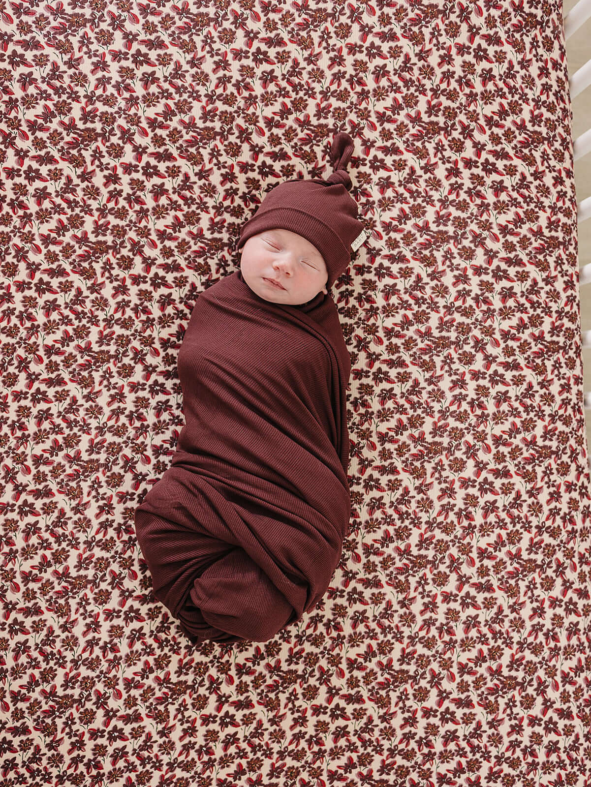 Cozy baby wrapped in Deep Violet Ribbed Bamboo Stretch Swaddle on a floral crib sheet.