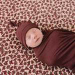 Newborn in Deep Violet Ribbed Bamboo Newborn Knot Hat, peacefully swaddled on floral blanket, perfect for milk & baby.