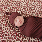 Newborn in Deep Violet Ribbed Bamboo Newborn Knot Hat, peacefully swaddled on floral blanket, perfect for milk & baby.
