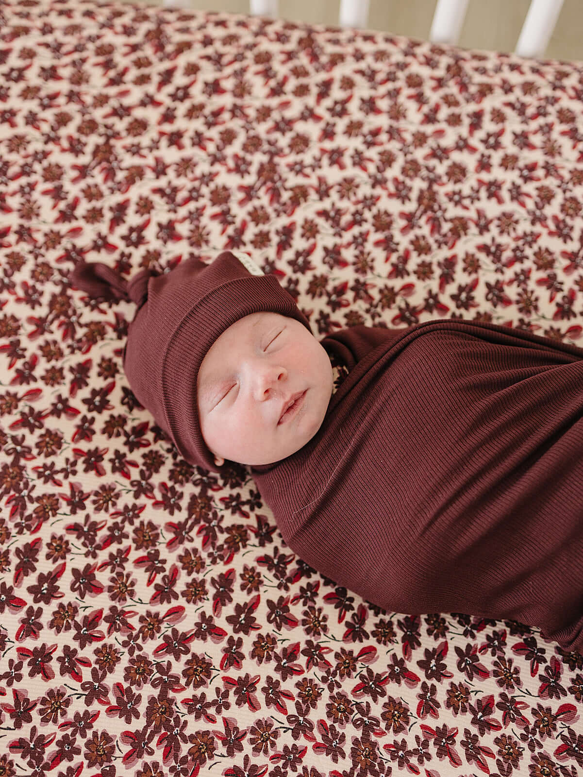 Newborn in Deep Violet Ribbed Bamboo Newborn Knot Hat, peacefully swaddled on floral blanket, perfect for milk & baby.