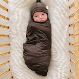 Brown Ribbed Bamboo Newborn Knot Hat on a wrapped baby in a cozy cradle