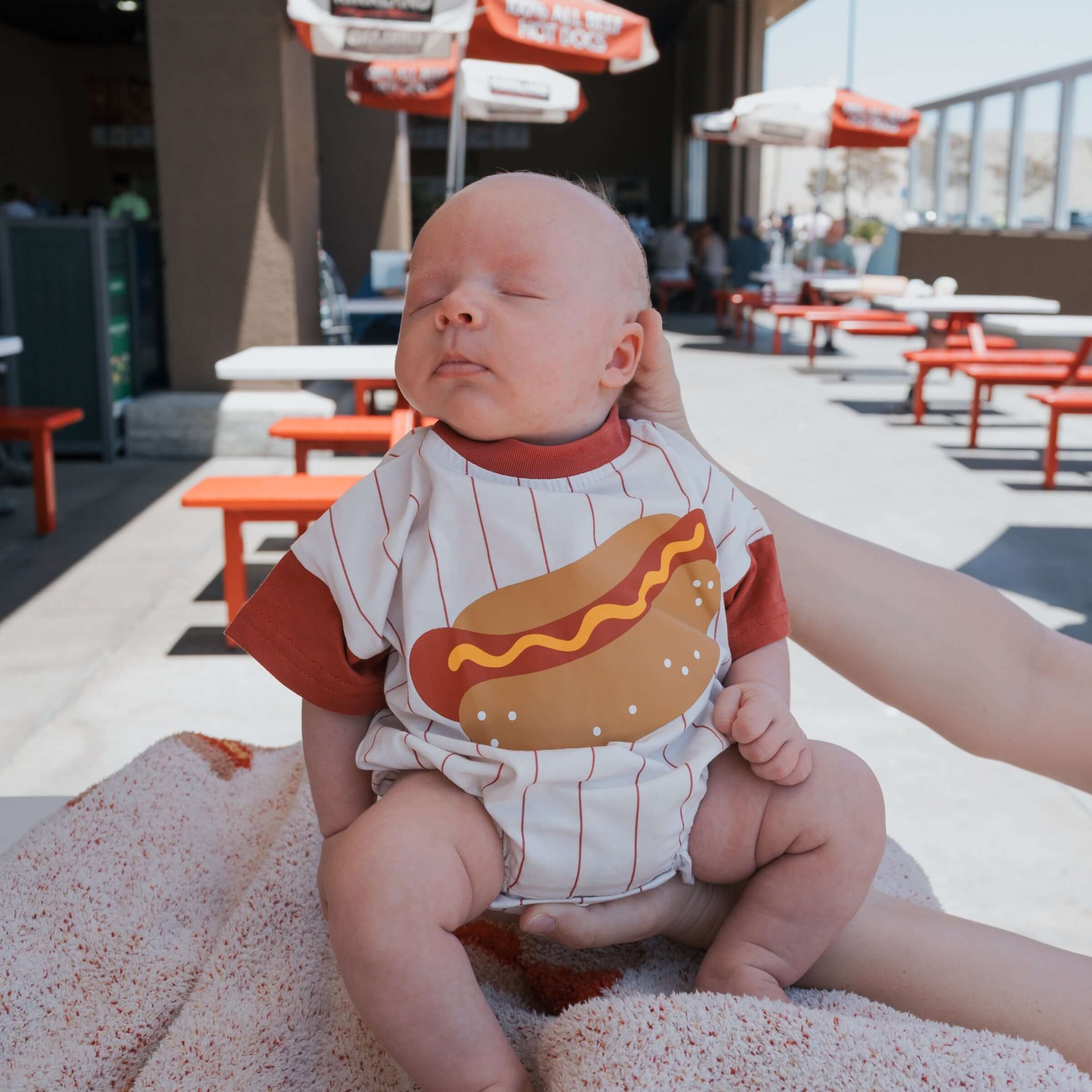 Baby wearing Hot Dogs | Short Sleeve Romper with a fun hot dog graphic outdoors.