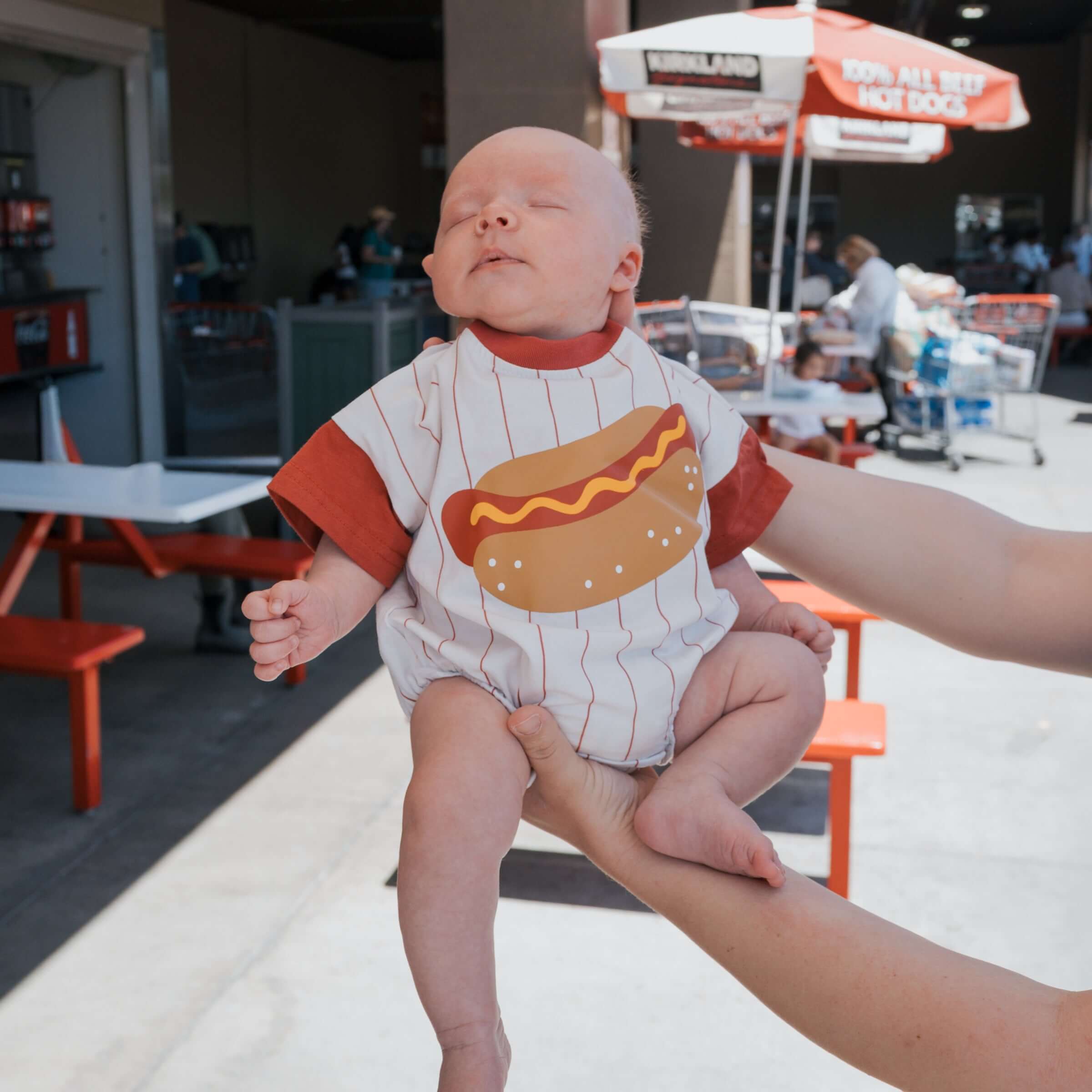 A baby wearing a Hot Dogs | Short Sleeve Romper with a cute hot dog graphic, perfect for fun outings.