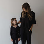Two people wearing black pajamas standing against a plain background