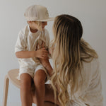 Woman and child sitting together on a chair, both wearing light-colored clothing.