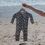 Bamboo Zip Pajamas displayed on a hanger at the beach, showcasing a stylish black and white pattern.