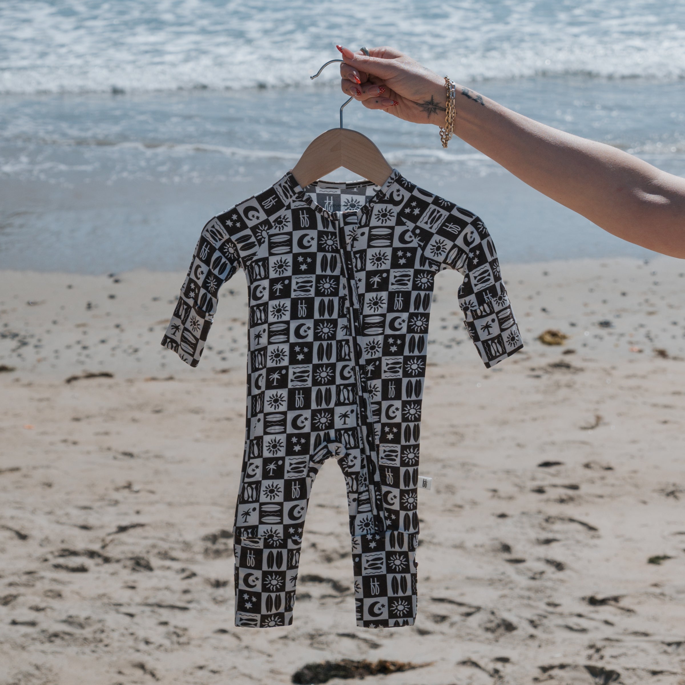 Bamboo Zip Pajamas displayed on a hanger at the beach, showcasing a stylish black and white pattern.