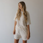 Woman wearing a white textured outfit against a plain background