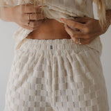 Person wearing a textured beige top and pants with a visible brand logo.
