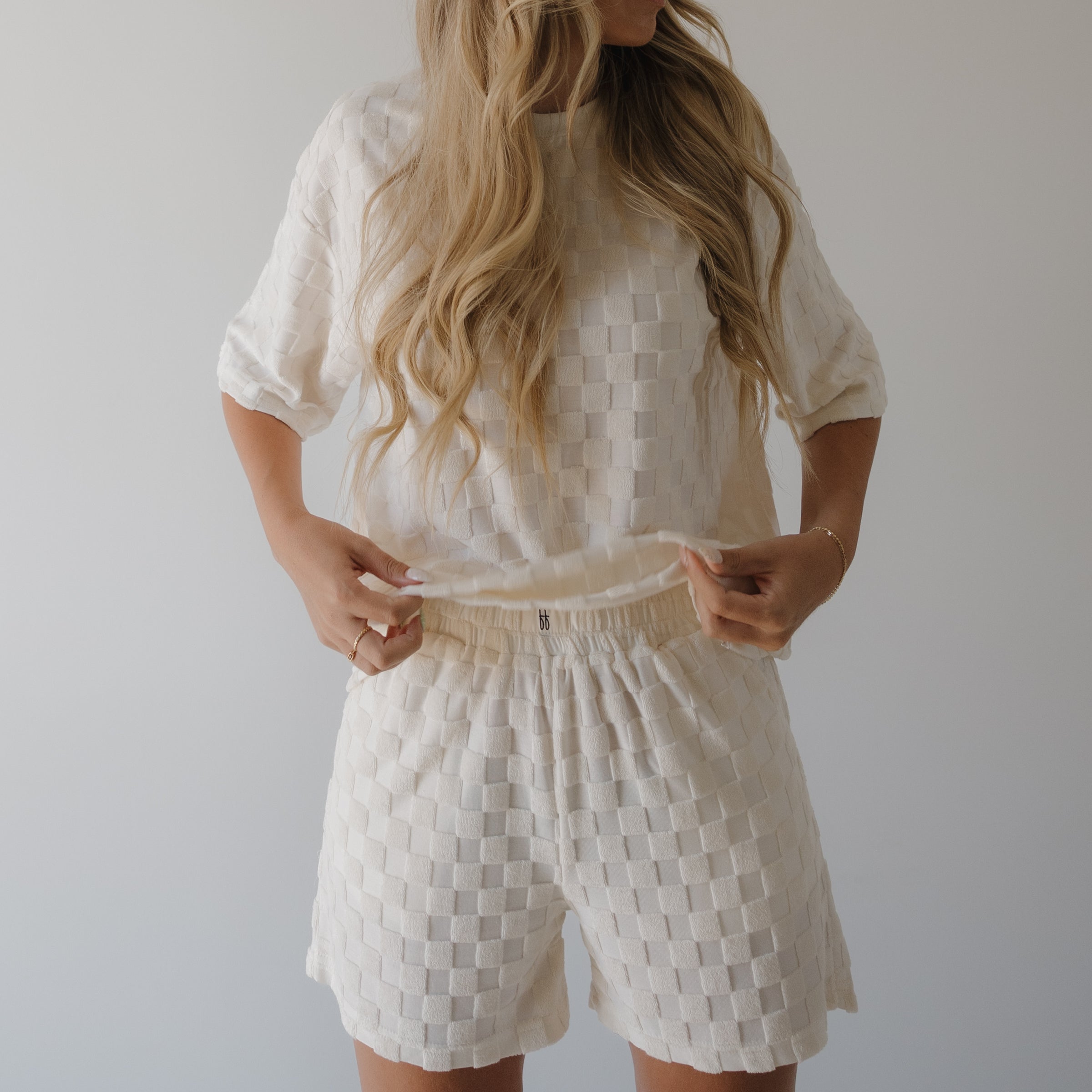 Person wearing a white textured outfit with shorts against a plain background