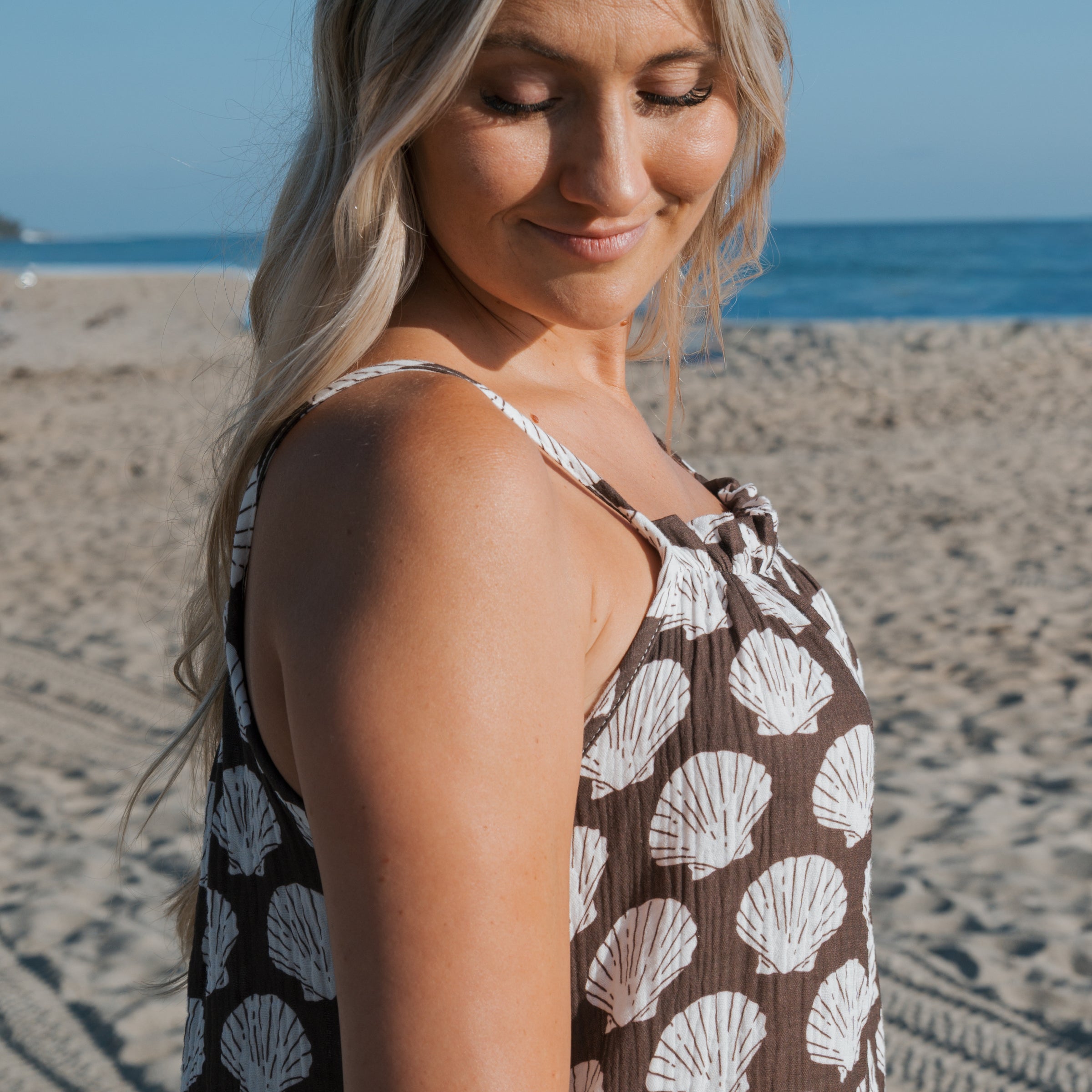 Woman wearing a Seashell Print Dress on the beach, showcasing a Women's Muslin Sleeveless Dress with a coastal vibe.