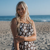 Woman wearing a seashell print Women's Muslin Sleeveless Dress at the beach with ocean view.