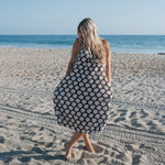 Woman wearing a Women's Muslin Sleeveless Dress with seashell print standing on the beach by the ocean.