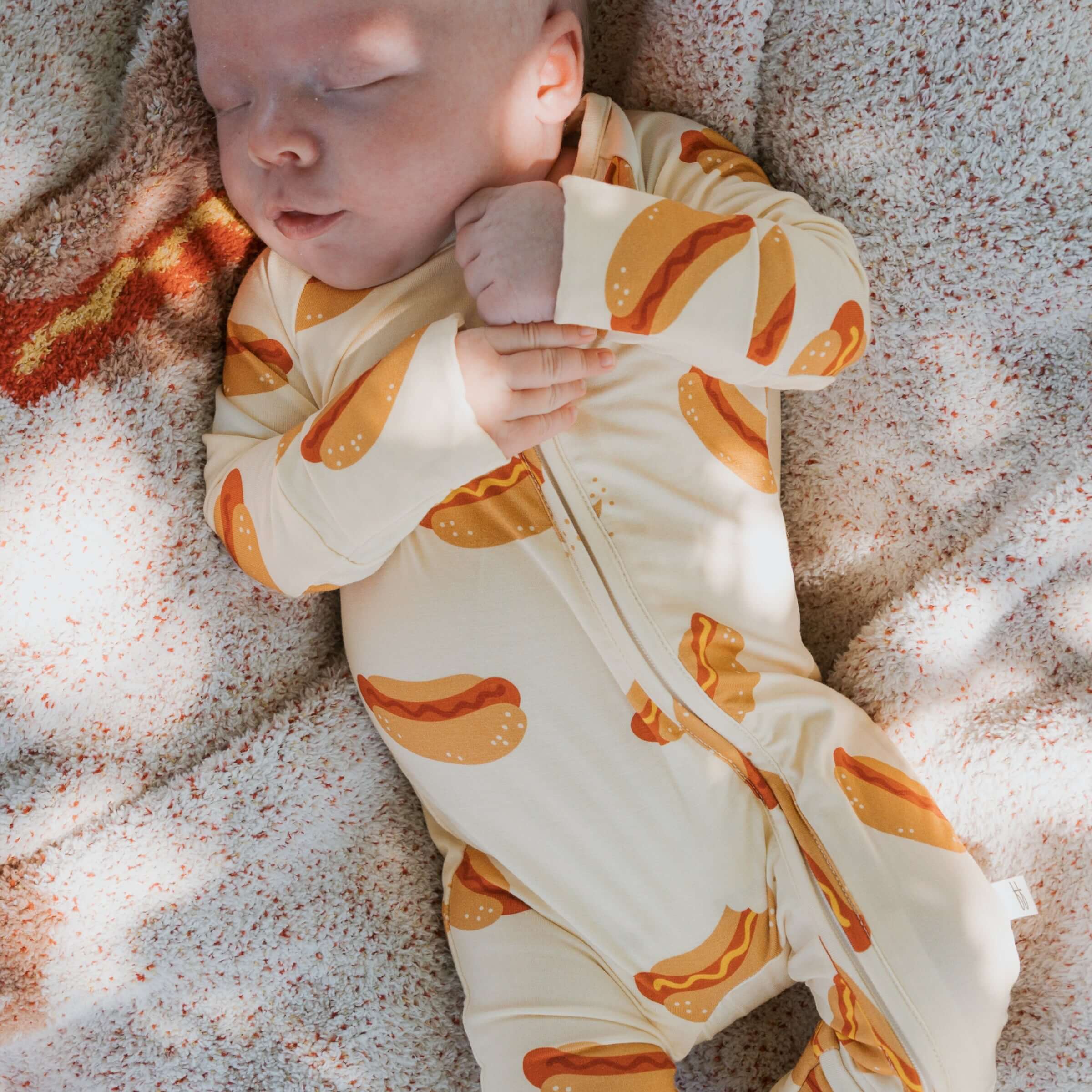 Baby peacefully sleeping in Hot Dogs | Bamboo Zip Pajamas with playful hot dog print on cozy fabric.