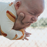 Baby in Hot Dogs | Bamboo Zip Pajamas, held by an adult, in a playful outdoor setting.