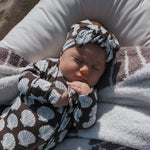 Newborn baby wrapped in a brown and white patterned blanket with a matching headband.