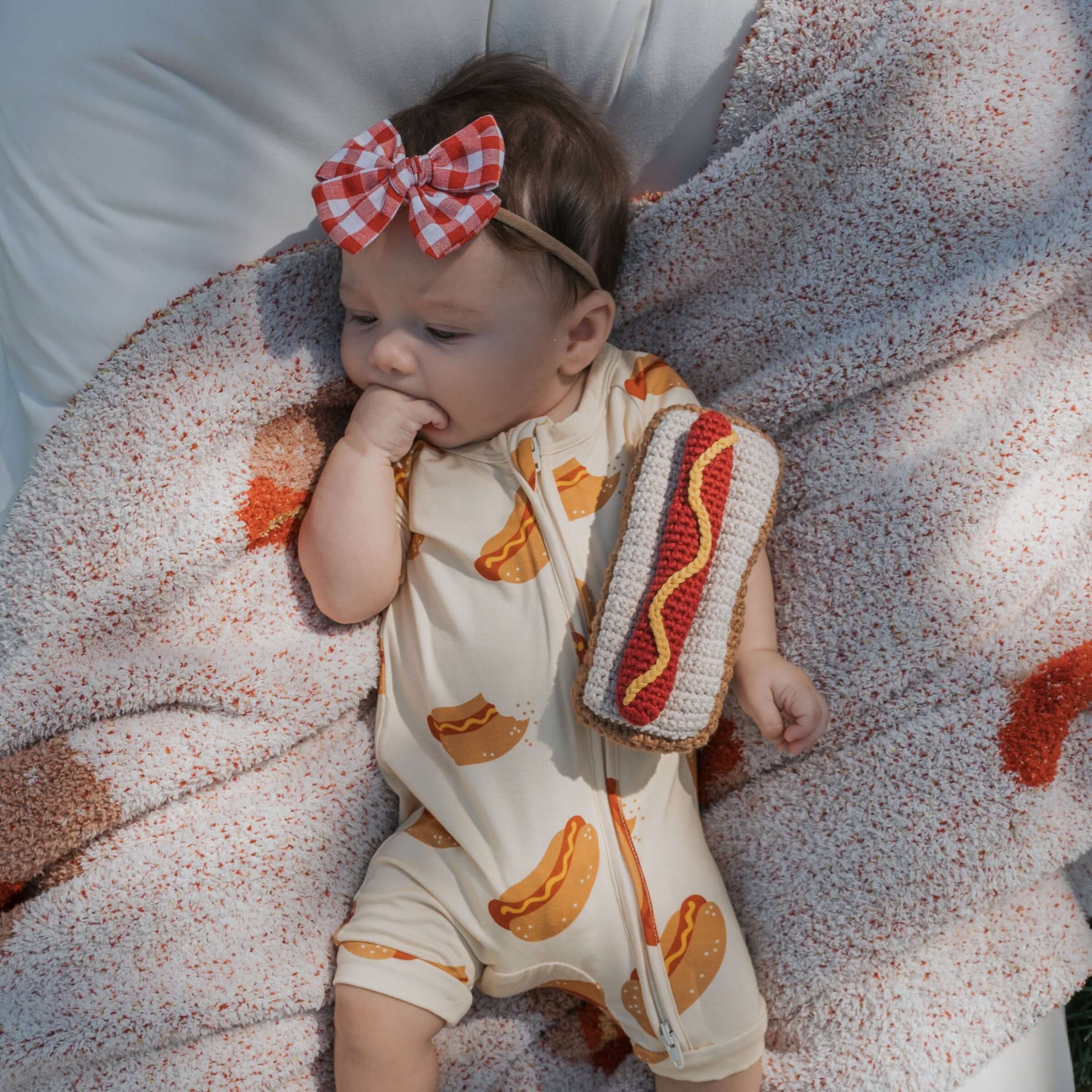 Baby enjoying summer with a Knit Rattle | Hot Dog in a cozy outfit and a stylish bow headband.