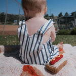 A baby sitting on a blanket with a Knit Rattle | Hot Dog, enjoying a sunny day outdoors.