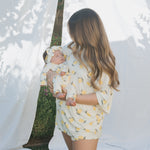 Woman holding a baby wrapped in a lemon-patterned zip outdoors.