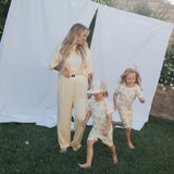 Woman and two children in matching outfits standing outdoors with white fabric in the background