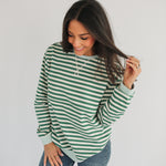 Woman wearing a green and white striped long-sleeve shirt and jeans on a plain background